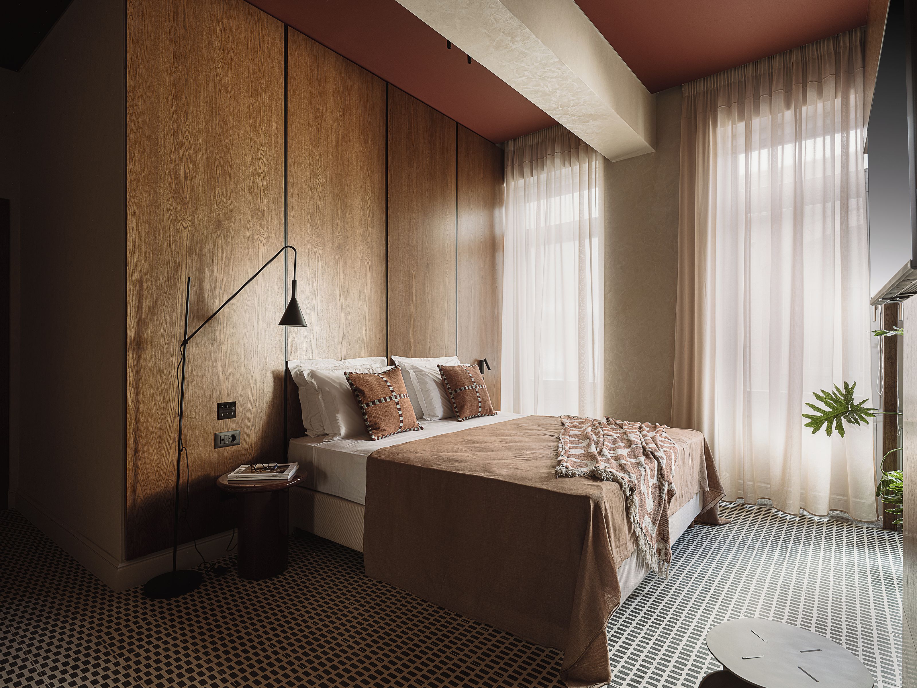 Une chambre à coucher avec un lit, une table de chevet, une lampe, des rideaux et une plante en pot.