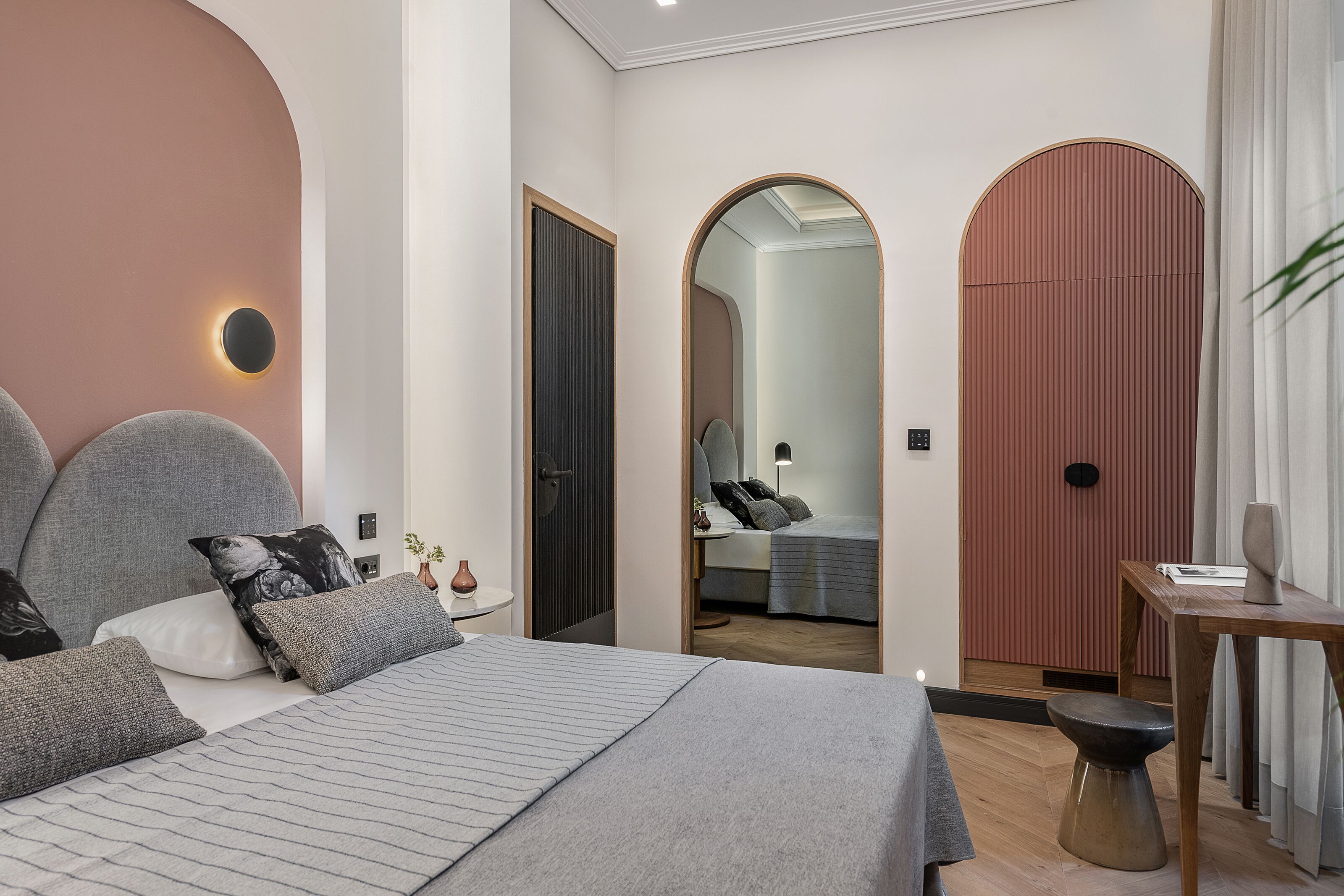 A modern bedroom with a large bed, a bedside table, a mirror, and a door leading to another room.
