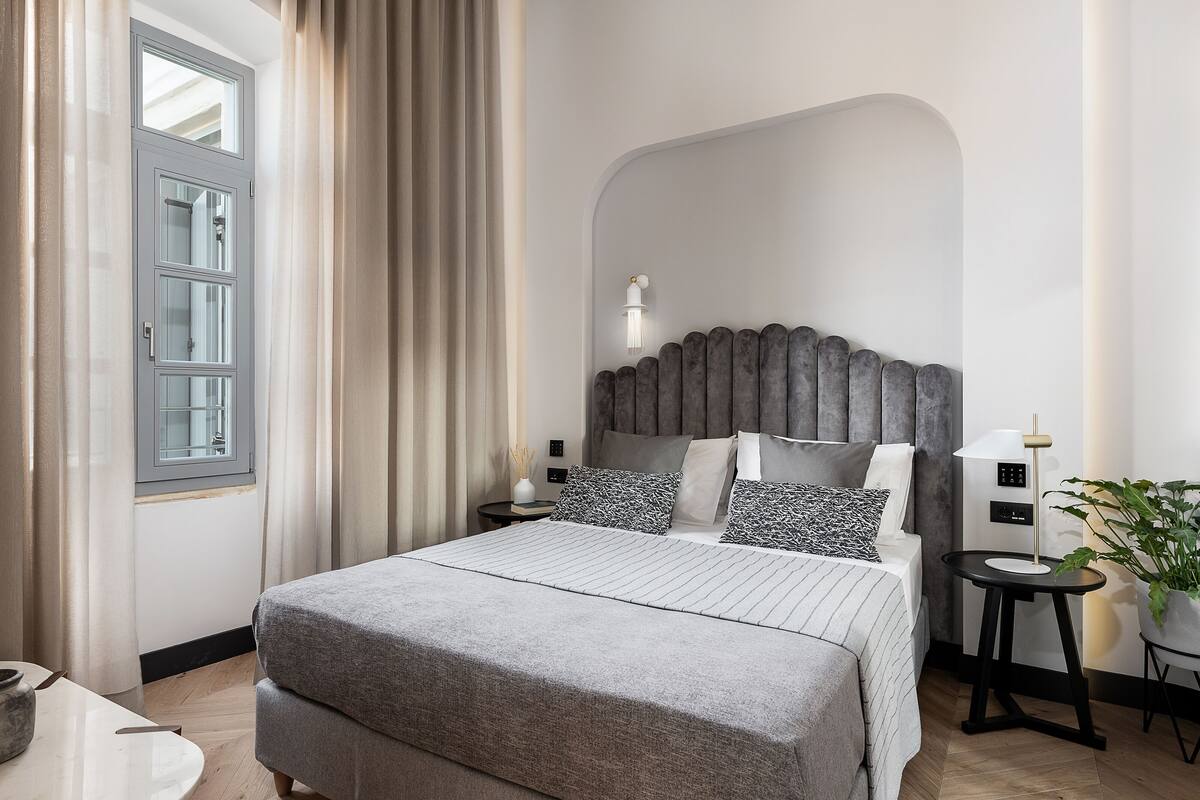 A modern bedroom with a large bed, a headboard, bedside tables, a lamp, and a potted plant.