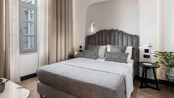 A modern bedroom with a large bed, a headboard, bedside tables, a lamp, and a potted plant.