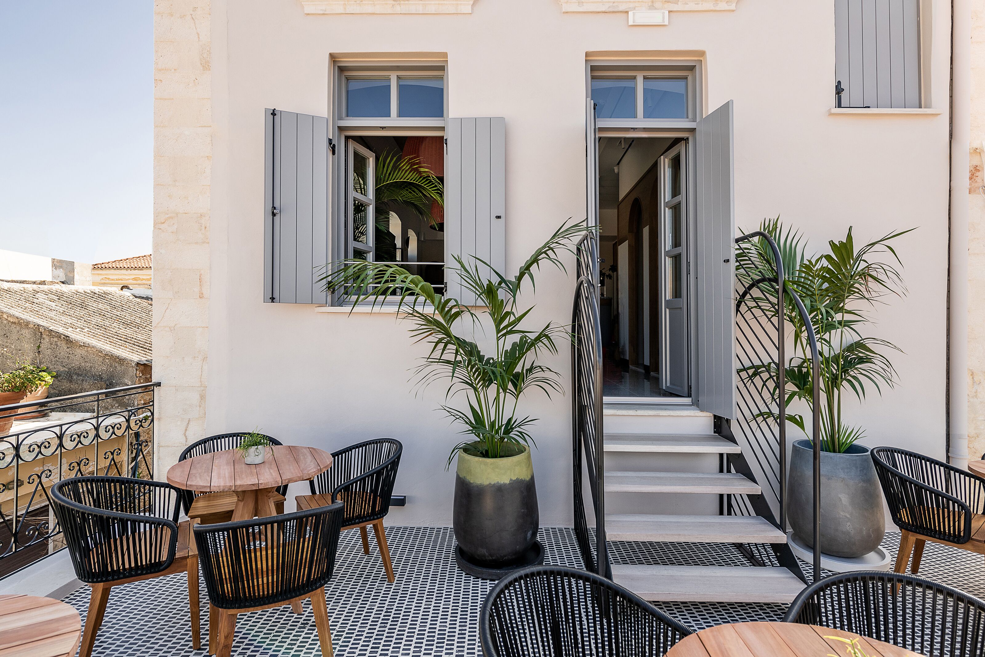 Un espace extérieur aménagé avec une table et des chaises, des plantes en pot et un escalier menant à un espace intérieur.