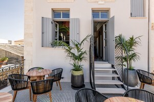 An outdoor seating area with a table and chairs, potted plants, and a staircase leading to an interior space.