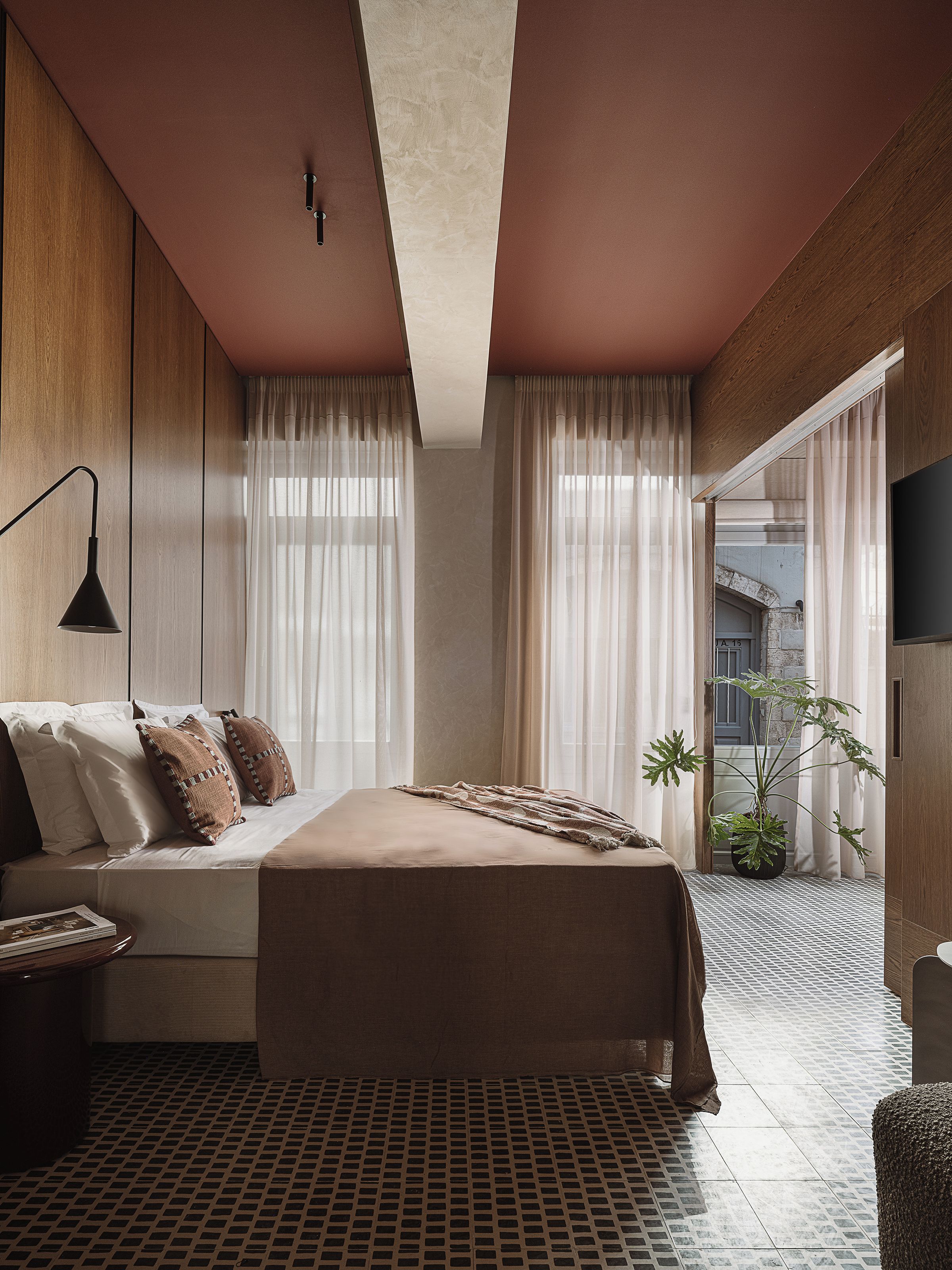 A modern bedroom with a large bed, a bedside table, a lamp, and a potted plant.
