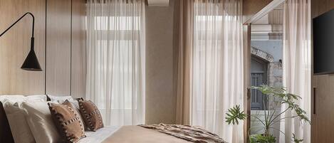 A modern bedroom with a large bed, a bedside table, a lamp, and a potted plant.
