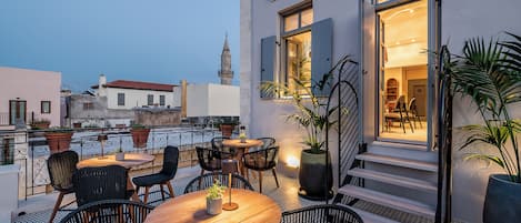 Una terraza en la azotea con mobiliario exterior, una escalera que conduce a una entrada y vistas de la ciudad.