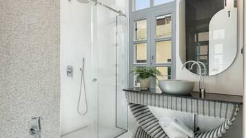 A modern bathroom with a glass-enclosed shower, a large mirror, and a striped bath tub.