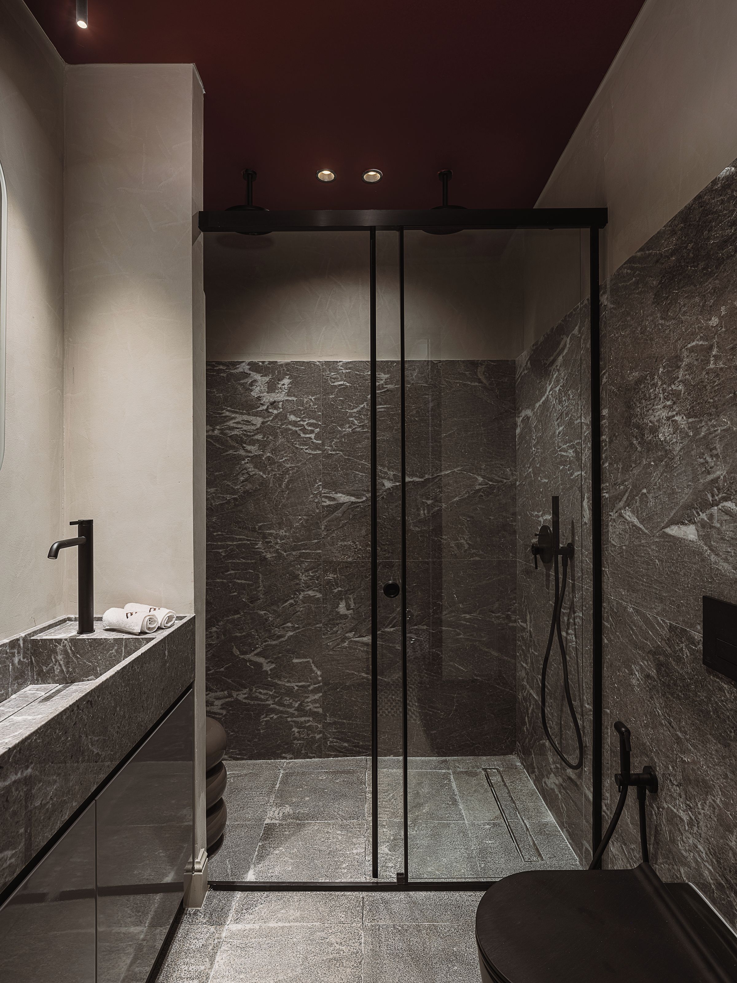A modern bathroom with a glass-enclosed shower, a marble-tiled wall, and a sink with a faucet.