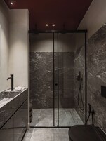 A modern bathroom with a glass-enclosed shower, a marble-tiled wall, and a sink with a faucet.