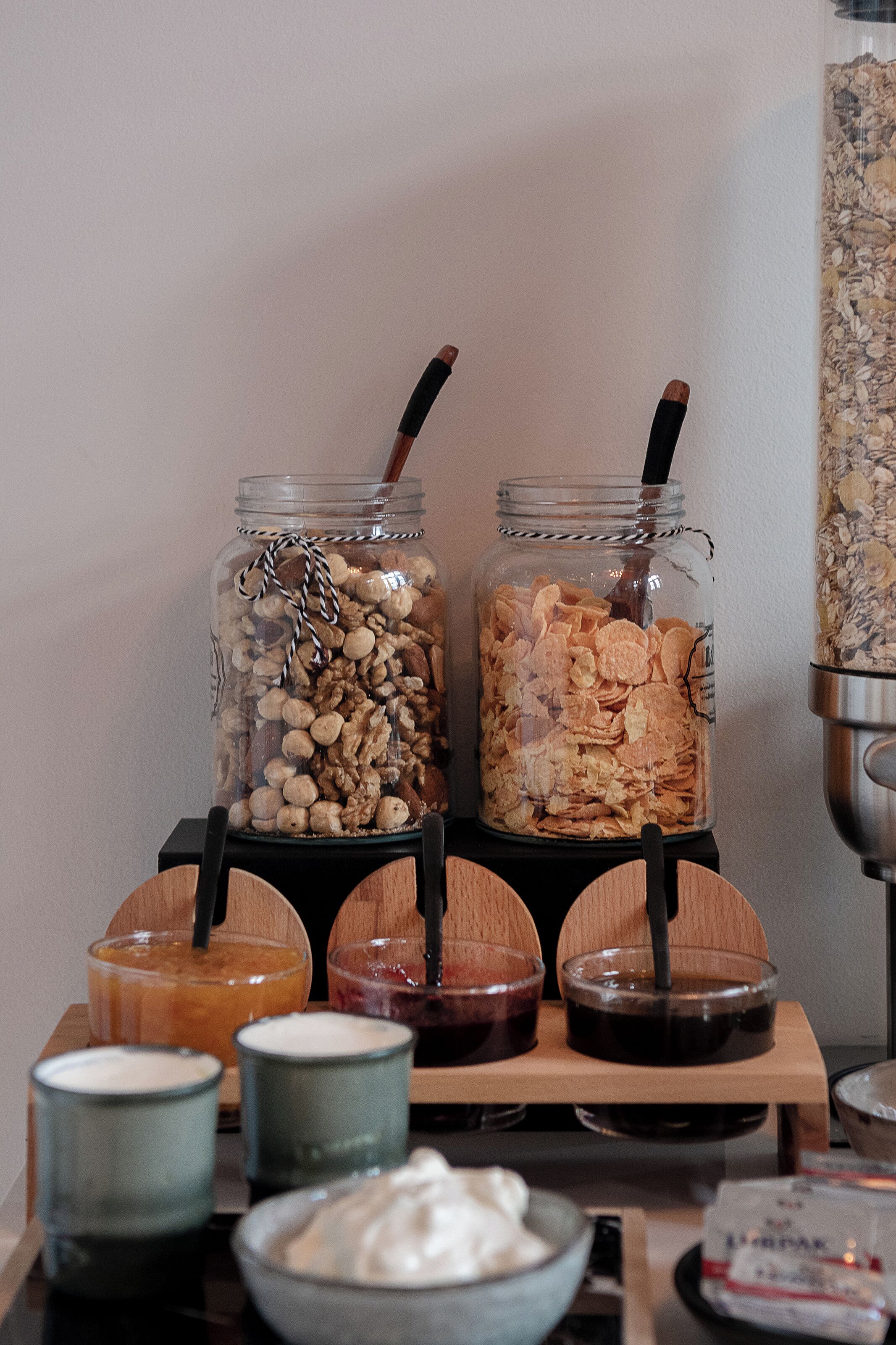 A breakfast buffet with jars of granola and nuts, bowls of yogurt, and a coffee machine.