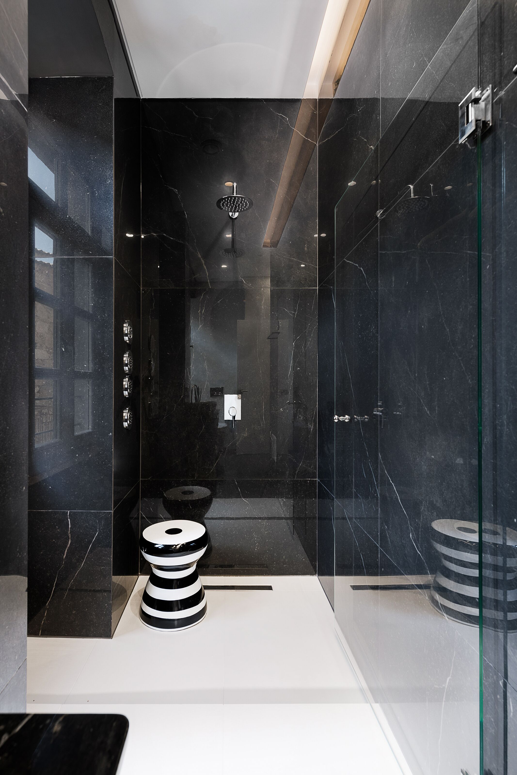 A modern bathroom with a glass-enclosed shower, a black marble wall, and a white sink.