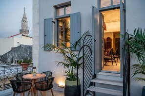 A balcony with a table and chairs, a potted plant, and a view of a building with a tower. - Malmo Historic Hotel (Chania)