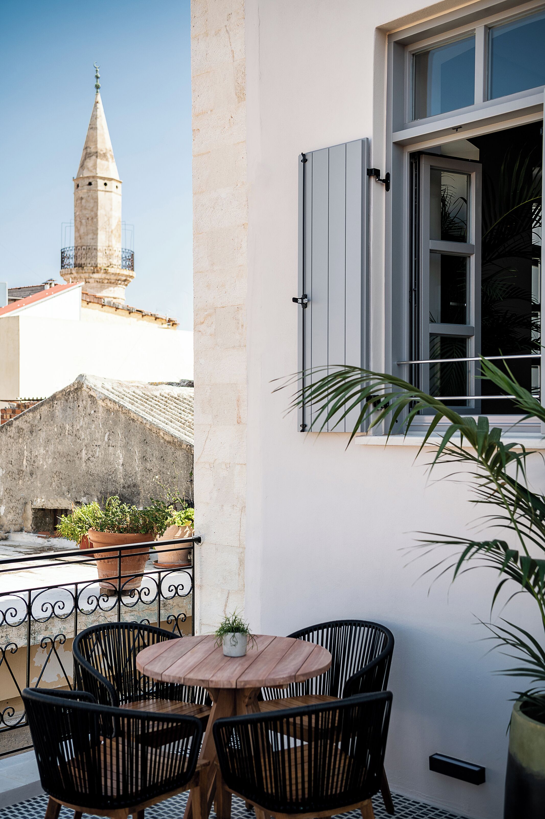 Un balcon avec une table et des chaises en bois, un pot de fleurs et une vue sur une tour.