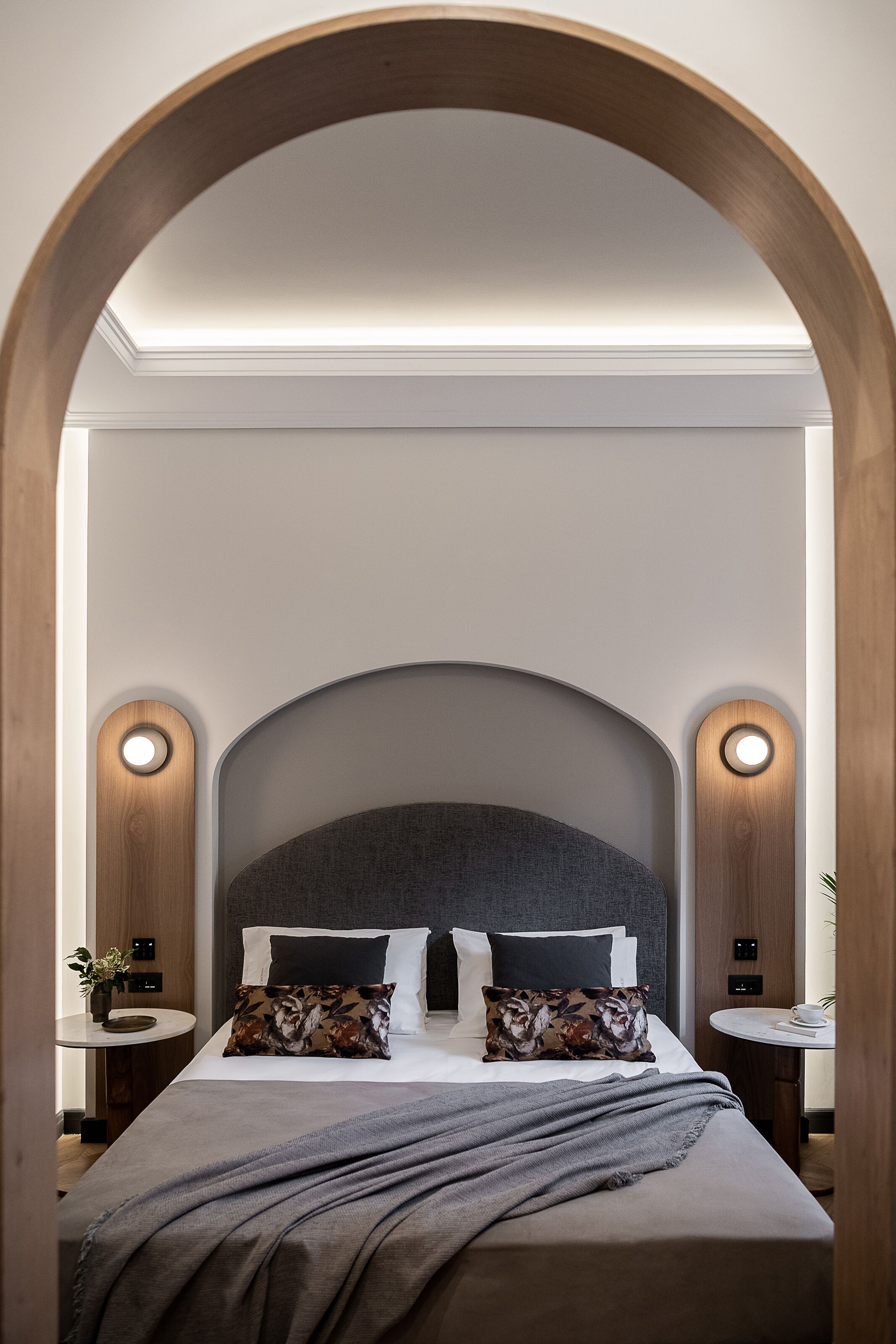 A modern bedroom with a large bed, two bedside tables, and a wooden arch above the bed.