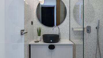 A modern bathroom with a glass shower enclosure, a round mirror, a black sink, and a pendant light.