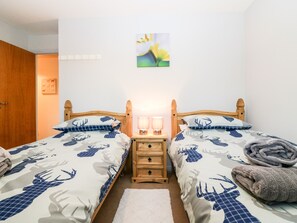 A double bed with a floral bedspread, a bedside table with a lamp, and a wooden headboard.
