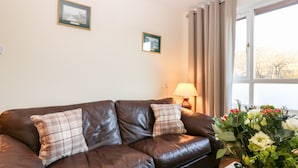 A brown leather sofa with plaid cushions, a table lamp, and a vase of flowers. - 10 Annesley Park (Banchory)