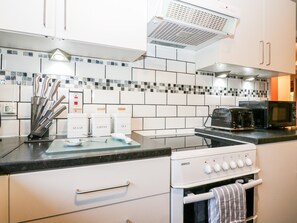 A modern kitchen with white cabinets, a black countertop, a Beko oven, a toaster, and a microwave.
