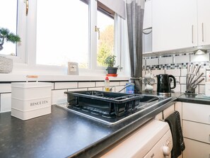 A modern kitchen with white cabinets, a black countertop, a sink, a coffee maker, and a potted plant. - 10 Annesley Park (Banchory)