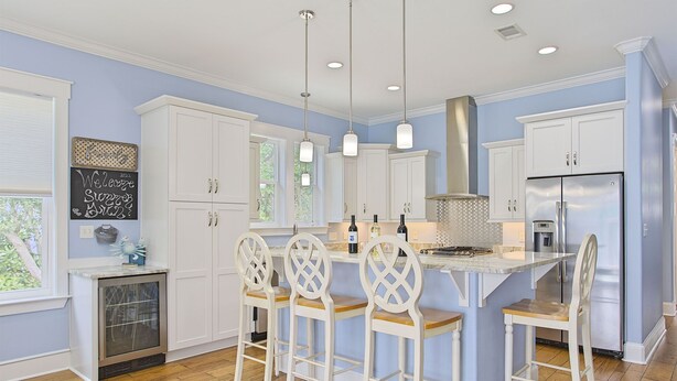 A modern kitchen with white cabinetry, a central island with bar stools, stainless steel appliances, and pendant lighting. - Aqua Waters - Newly Updated Vacation Home with Golf Cart, Private Pool + Cabana! (Destin)