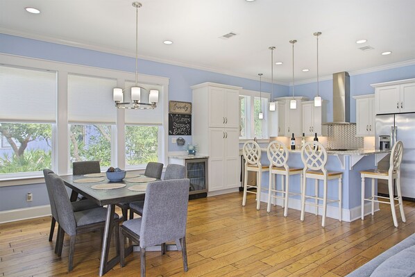 A modern kitchen with white cabinets, a central island with bar stools, and a dining area with a table and chairs.