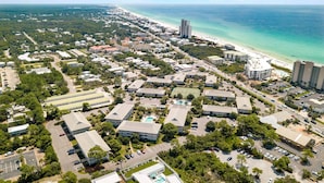 Vue aérienne d’une ville côtière avec des immeubles résidentiels, une plage et un grand hôtel doté d’une piscine.