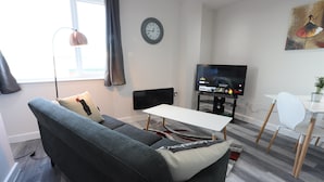 Ein modernes Wohnzimmer mit einem grauen Sofa, einem weißen Tisch und einem Fernseher auf einem Lowboard.