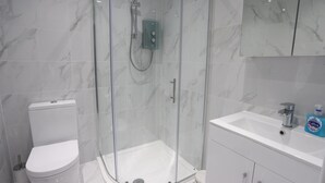 Ein modernes Badezimmer mit einer Glaskabine zur Dusche, einer weißen Toilette und einem Waschbecken mit Spiegel darüber.