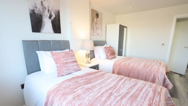 A hotel room with two beds, a nightstand, a lamp, and artwork on the walls. - Interchange14 - NEC Airport Interchange (Birmingham)