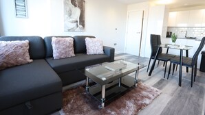 A modern living room with a sectional sofa, a glass coffee table, and a dining area with chairs and a table. - Interchange14 - NEC Airport Interchange (Birmingham)