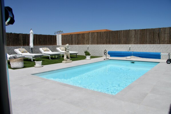 Une piscine avec des chaises longues et un petit espace aménagé en jardin.