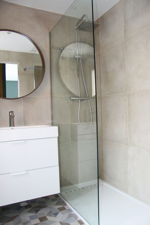 Une salle de bain moderne avec une douche à parois de verre, un miroir rond et un meuble-lavabo blanc.