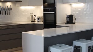 Una cocina moderna con una isla central, taburetes de bar, una cafetera y un hervidor.