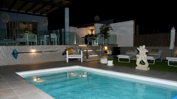 Una piscina con solárium empedrado, rodeada de sillones de descanso y una zona de estar exterior moderna.
