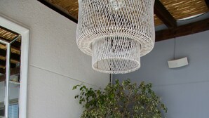 Un espacio exterior moderno con asientos, una mesa de centro de vidrio, cojines blancos y una planta en maceta.