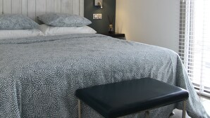 Un dormitorio con una cama grande, una mesita de noche, una lámpara y una ventana con persianas.