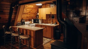 Una cocina tipo cabaña de madera con una isla central, taburetes de bar, microondas, estufa, fregadero y un cartel que dice 'Bienvenido a la cabaña'.