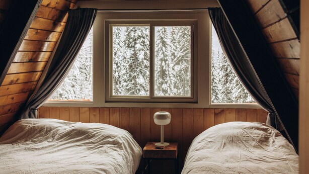 Un dormitorio acogedor en el ático con dos camas, una ventana con vistas a árboles, una alfombra estampada y un ventilador de techo.