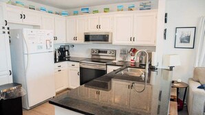 Cocina compacta con armarios blancos, refrigerador de acero inoxidable, microondas, horno y lavaplatos.