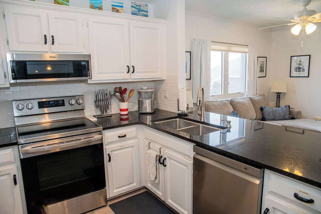 A modern kitchen with white cabinets, stainless steel appliances, and a black countertop.