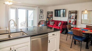 Una cocina moderna con lavavajillas integrado, un comedor con una mesa redonda y sillas, un sofá rojo y un televisor de pantalla plana montado en la pared.