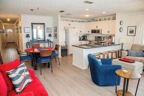 Una cocina moderna con armarios blancos, una isla central y un comedor con sillas rojas y una mesa.