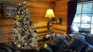Accogliente interno di una baita con un albero di Natale addobbato, mobili in pelle e una finestra vista su un paesaggio innevato.