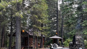 Un rustico chalet in legno con veranda e zona relax esterna, circondato da alberi alti.