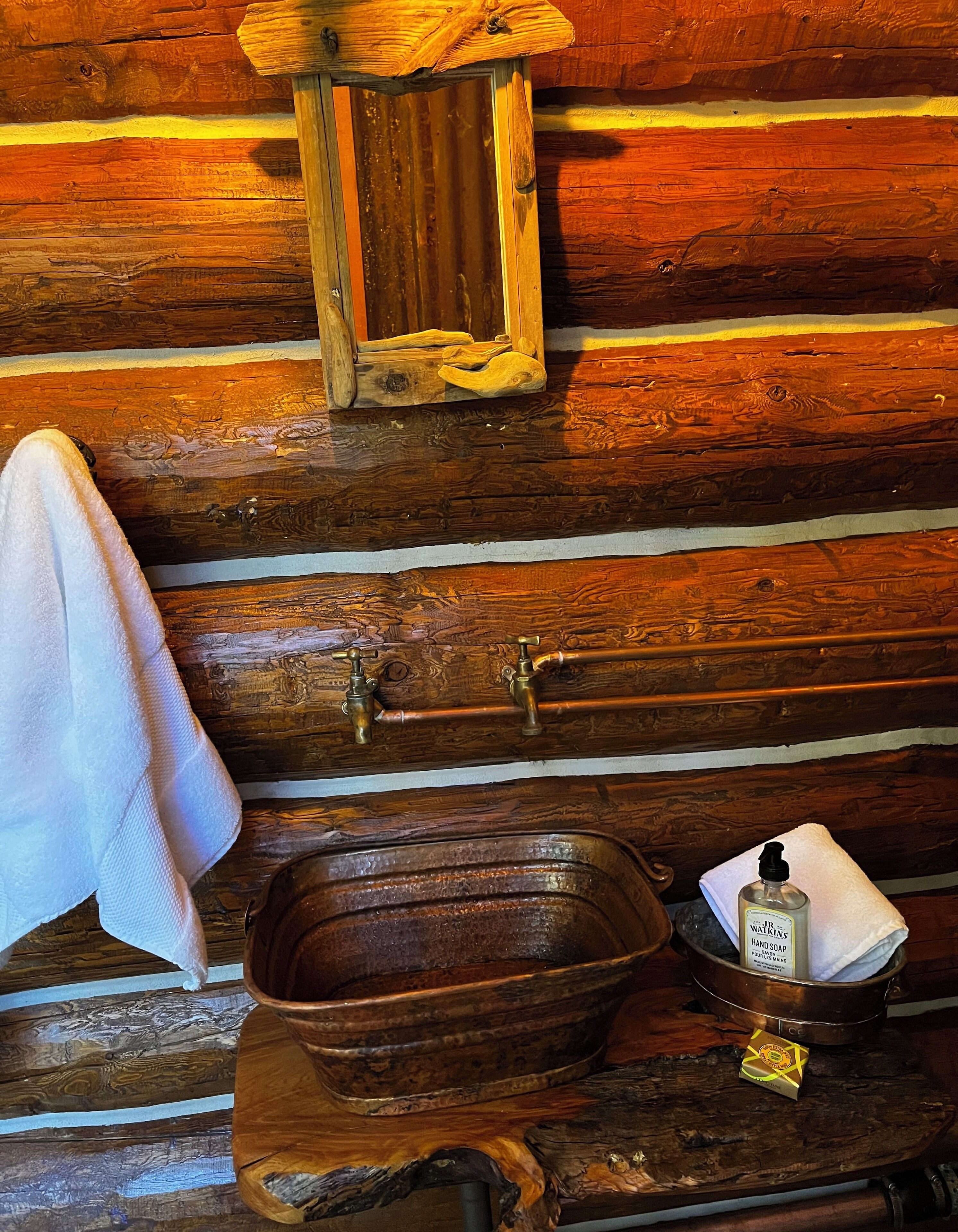 L’intérieur d’un chalet rustique en bois, avec un lavabo en bois, une serviette et un flacon de savon pour les mains.