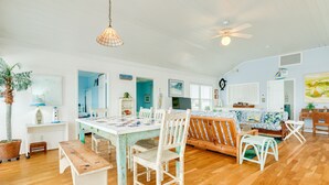 Amplia sala de estar con mesa de comedor de madera, sillas blancas, un sofá y un ventilador de techo.