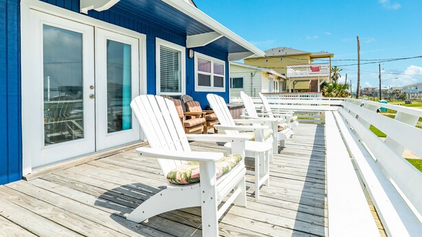 Una terraza de madera con sillas Adirondack blancas y un área techada con barandilla.