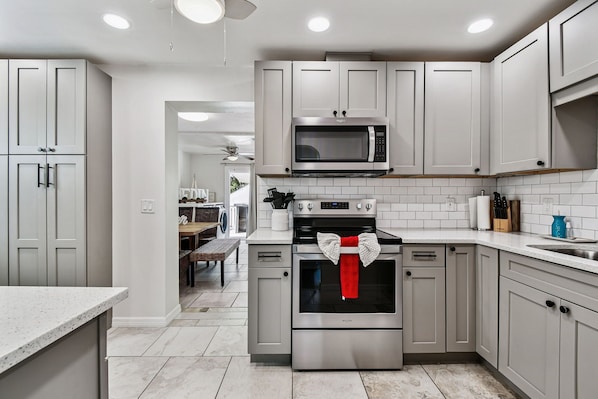 A modern kitchen with stainless steel appliances, white cabinetry, and a tiled backsplash.