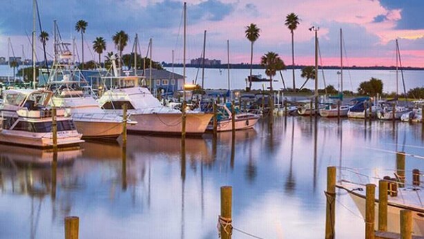 A marina with boats docked, calm water, and a sunset in the background.