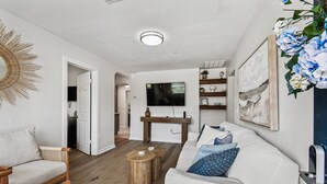 A modern living room with a white sofa, wooden coffee table, and a TV mounted on the wall.