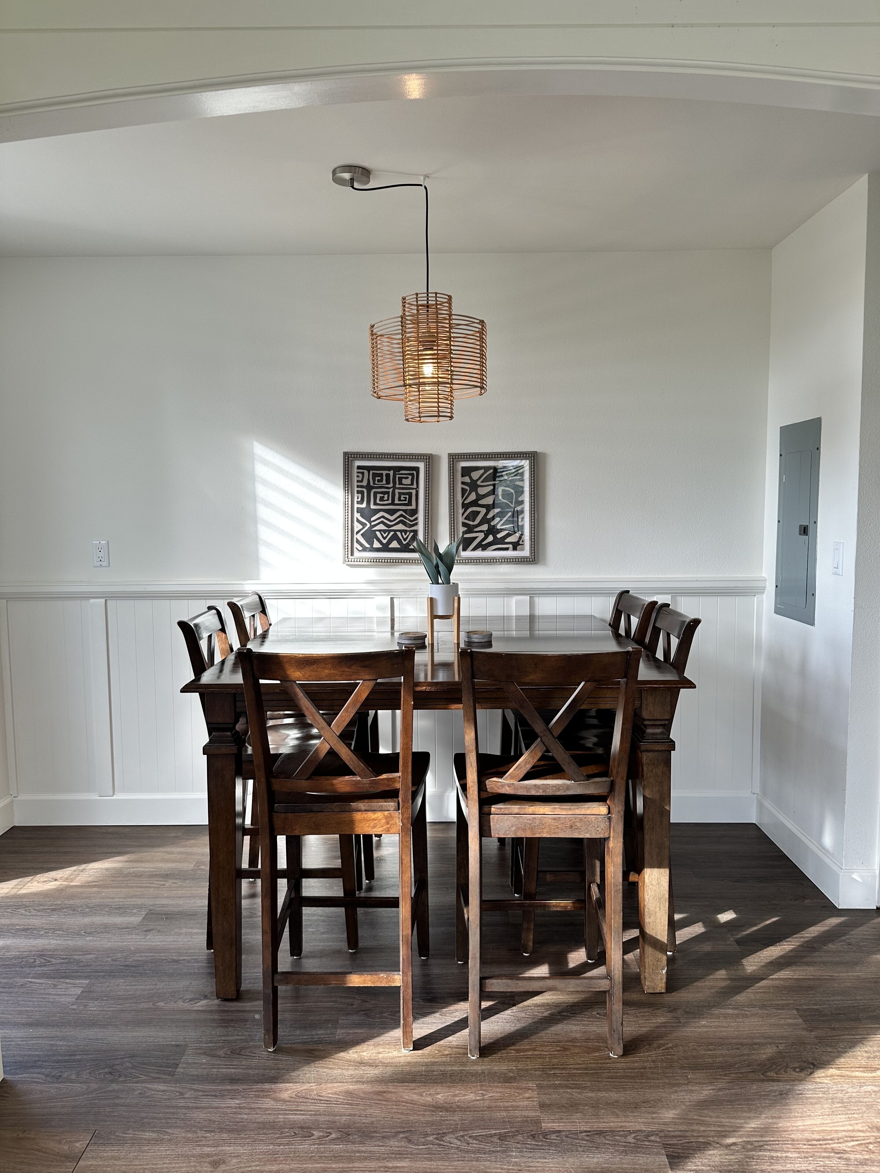 Un comedor con mesa y sillas de madera, una lámpara colgante y dos obras de arte enmarcadas.